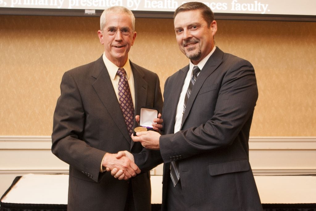 Dr. Nicholas Benson, Vice Dean for the Brody School of Medicine presents a Laupus medallion to book author, Roger Russell, Assistant Director of User Services for Laupus Library. (Photo by Layne Carpenter)