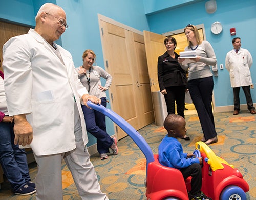 Pediatric cardiologist Dr. Charlie Sang pushes his patient, Elijah, in a toy car the day before he travels home to Uganda.