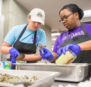 At left, Brianna Harrington, a junior from Waxhaw, and Lekisha Pittman, a senior from High Point, prepare meals for Greenville children by volunteering with Campus Kitchen at ECU.