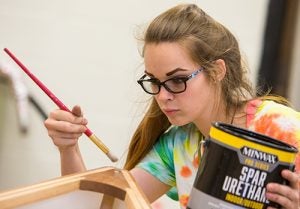 Student Ella Snow puts a coat of urethane on her canoe before going to the common.