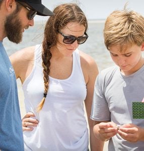 Autumn Reaghard, a teacher at Cape Hatteras Secondary School, examines a small crab with instructor David Sybert, K-12 education specialist at the UNC Coastal Studies Institute, and camper Pierce Chase, 11, from Kitty Hawk.