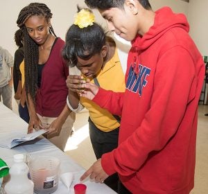 ECU student Nina Franklin monitors an experiment being conducted by Tatiyanna Berry, age 14, and Mariano Galvan Rojas, age 14.