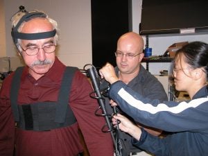 East Carolina University Graduate students James Crouch and Xiaozheng Yao assist Professor Moha Tabrizi as he tries on a body motion capture device, a set of sensors that tracks movements of the human body