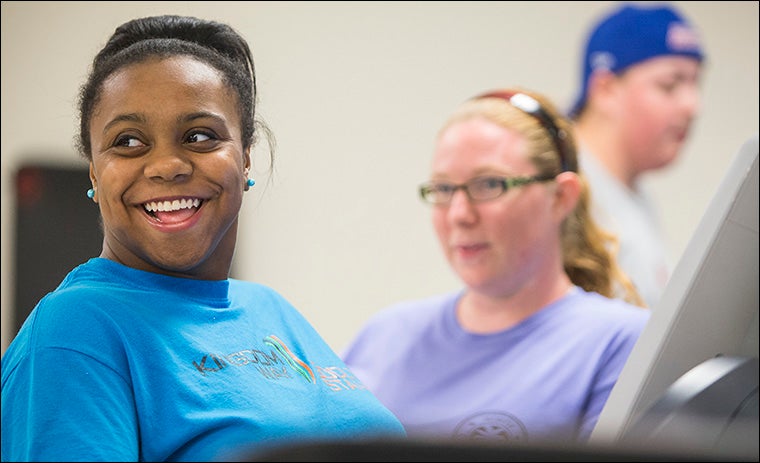 Project Mentor participant Faithful-Joy Cotton smiles while working out on a recumbent bicycle. At right is Cotton's mentor, Shayna Meyers.