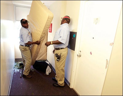 Franklin Andrews and Henry Henderson, ECU Facilities Services, remove mattresses and tables used to block a broken window in Greene residence hall.