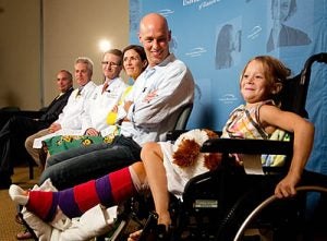 Lucy Mangum, 6, smiles for the cameras Tuesday as she, her parents and Dr. Richard Zeri, third from left, talk about last week's shark attack in Ocracoke, which injured Lucy's leg. Photos by Cliff Hollis