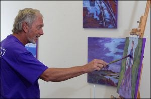 John Groesser applies purple acrylics to a painting at the artists' studio.