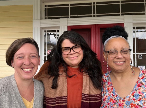 Three woman stand together in front of a door.