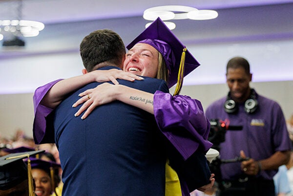A young woman hugs a young man wearing a military uniform with his back to the camera.