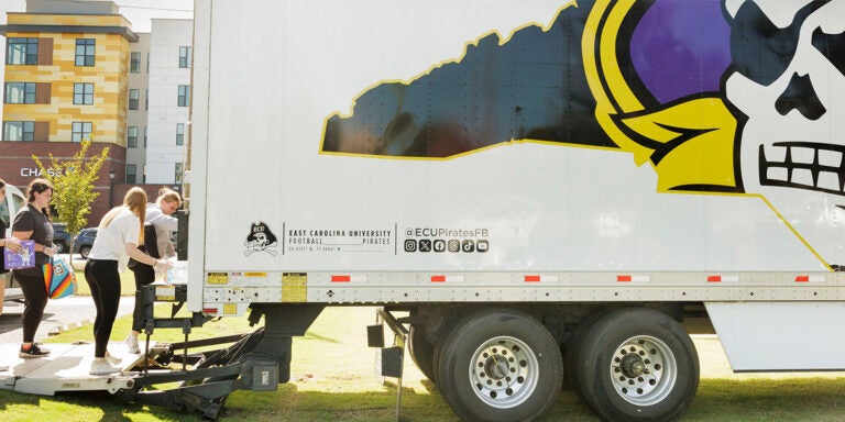 A woman places a case of water in a semi-trailer with the ECU athletic logo on the side.