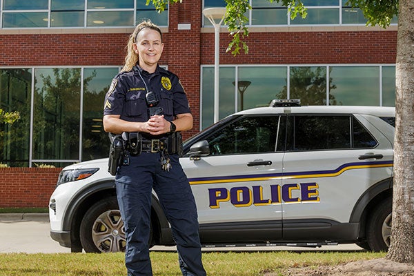 : A uniformed police officer for East Carolina University stands in front of her patrol car on campus. 