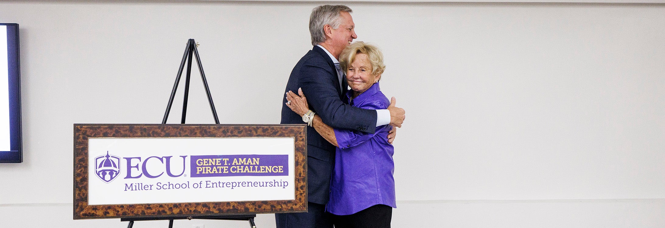 Fielding Miller hugs Helen Aman standing next to a sign.