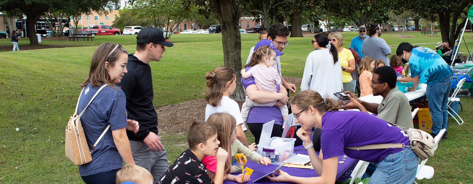 Families and children from the local community visit a table with exhibits staffed by East Carolina University students outside on the green lawn of the Town Common in Greenville, North Carolina, in 2023.