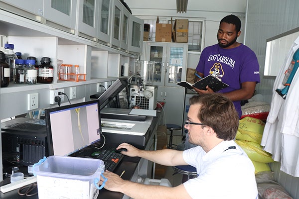 ECU students Thomas Thornburg (seated) and Kyle Davis (standing) photograph and analyze the root of a peanut plant.