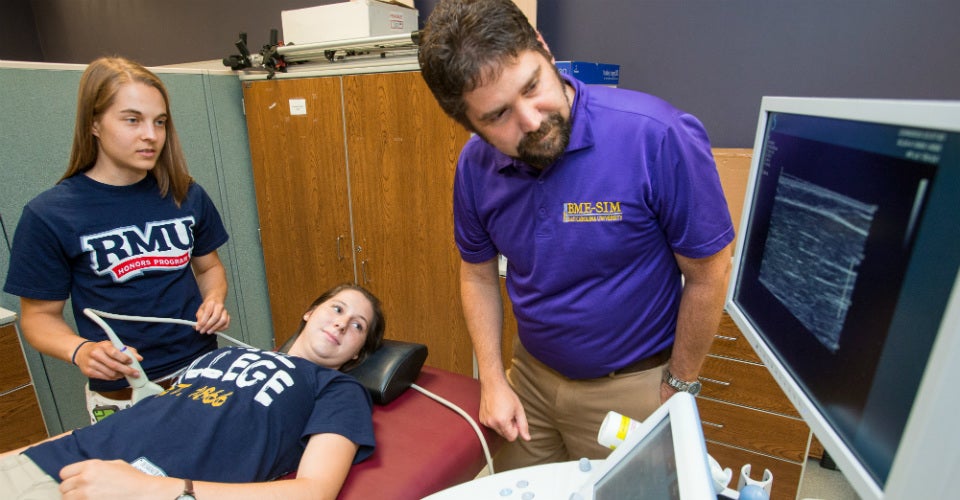 REU students use ultrasound to study arm movements. Dr. Zachary Domire, associate professor in the ECU Department of Kinesiology, works with Jennifer Rickens, an undergraduate student at Thiel College, on table, and Kylee Schaffer, 
a Robert Morris University student. Rickens is getting a muscle ultrasound. 
(Photos by Cliff Hollis)