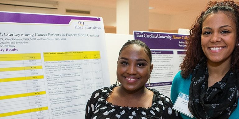 Chelsey Turner, left, and Cheyenna Francis pose with their poster detailing their research into medication adherence and health literacy among cancer patients. (Photos by Cliff Hollis; videos by Rich Klindworth)