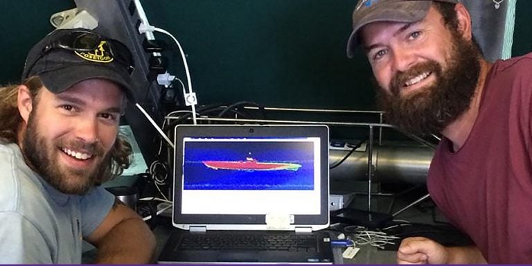 ECU alumni John Bright, left, and Joe Hoyt are shown with an image of the German submarine they discovered using location techniques Bright developed. (Photo by Brandi Carrier, Bureau of Ocean Energy Management)