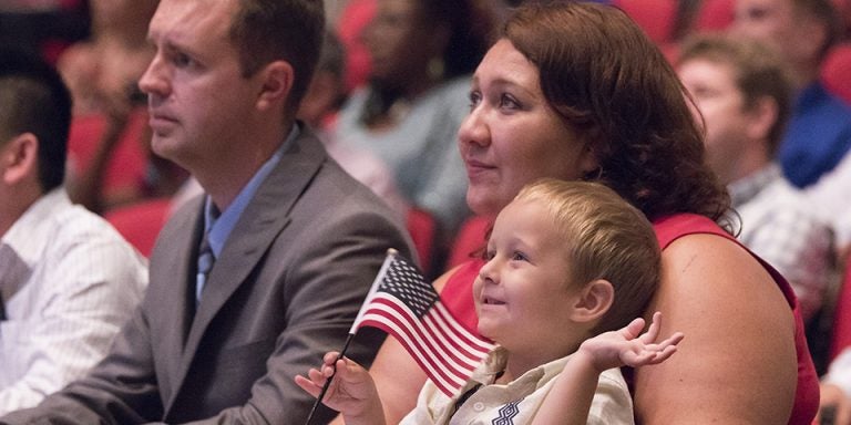 Daniel Feterovskiy waves a flag as his mother Oksana Feterovkaya and father Aleksy Feterovskiy (last names vary because of gender) listen to a video message from President Barack Obama. The couple immigrated to the U.S. from Uzbekistan and were at ECU to participate in a naturalization ceremony. (Photos by Jay Clark)