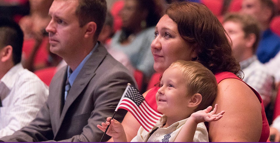 Daniel Feterovskiy waves a flag as his mother Oksana Feterovkaya and father Aleksy Feterovskiy (last names vary because of gender) listen to a video message from President Barack Obama. The couple immigrated to the U.S. from Uzbekistan and were at ECU to participate in a naturalization ceremony. (Photos by Jay Clark)