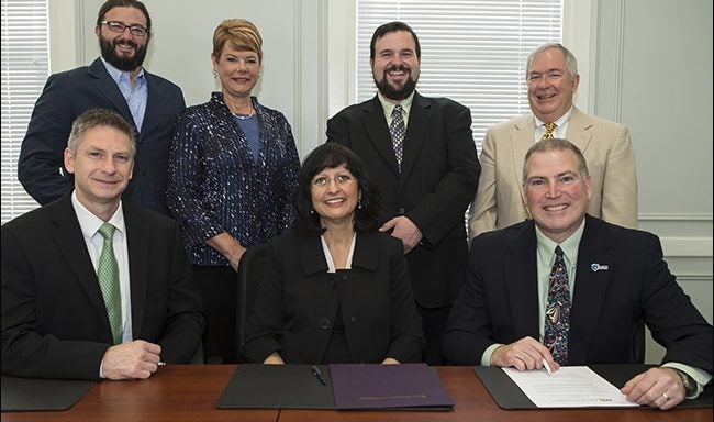 Seated center front, ECU Honors College Dean Marianna Walker prepares to sign an agreement with DSM Dyneema site director Jim Lawless, right, and DSM Dyneema engineering director Scott Quinn, at left. The Greenville fiber manufacturer will fund an EC Scholar award earmarked for an engineering student. Standing left to right, Todd Fraley, director of the EC Scholars Award Program; Deb Mungal, director of DSM’s Human Resources & Training; Ricky Castles, assistant professor of engineering; and Hayden Griffin, professor and chairman of the Department of Engineering. (Photo by Cliff Hollis)