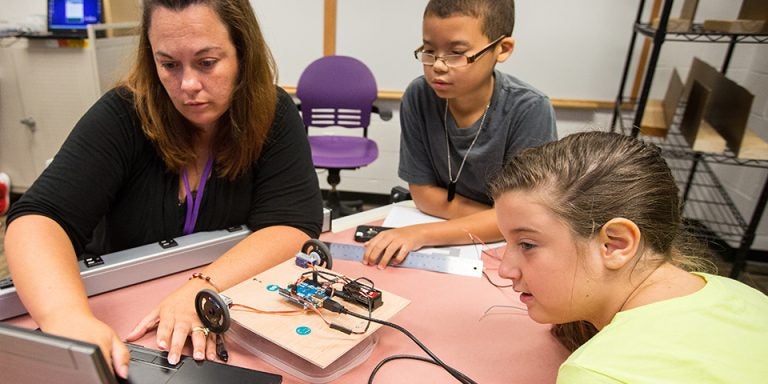 Left to right, Shelley Tripp, a teacher at Bethel School, keys in information for a robot she built with rising seventh-graders Daeshawn Smith and Alyssa Mayo during the inaugural Advanced Manufacturing and Innovation Academy held at ECU. The entrepreneurship, science, technology, engineering, art and design and math or eSTEAM academy was funded by a $1.25 million Golden LEAF Foundation grant. (Photo by Cliff Hollis)