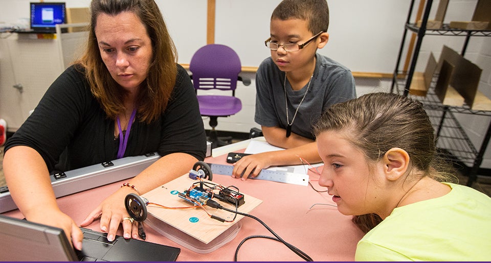 Left to right, Shelley Tripp, a teacher at Bethel School, keys in information for a robot she built with rising seventh-graders Daeshawn Smith and Alyssa Mayo during the inaugural Advanced Manufacturing and Innovation Academy held at ECU. The entrepreneurship, science, technology, engineering, art and design and math or eSTEAM academy was funded by a $1.25 million Golden LEAF Foundation grant. (Photo by Cliff Hollis)