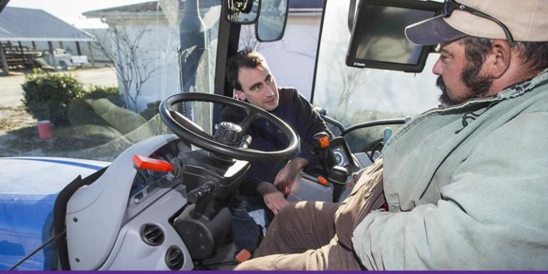 ECU graduate student Matt Gallagher, left, talks with an equipment operator at Cherry Research Farm in Goldsboro as part of a N.C. Agromedicine Institute program to improve operator comfort. ECU's involvement in the Agromedicine Institute is one of the attributes that helped ECU earn the designation of an Innovation and Economic Prosperity University from the Association of Public and Land-grant Universities. (Photo by Cliff Hollis)