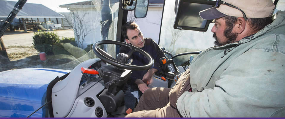 ECU graduate student Matt Gallagher, left, talks with an equipment operator at Cherry Research Farm in Goldsboro as part of a N.C. Agromedicine Institute program to improve operator comfort. ECU's involvement in the Agromedicine Institute is one of the attributes that helped ECU earn the designation of an Innovation and Economic Prosperity University from the Association of Public and Land-grant Universities. (Photo by Cliff Hollis)