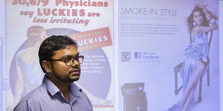ECU professor Dr. Vivek Anand has completed research that demonstrates a large number of teens in eastern North Carolina are using e-cigarettes, with minimal knowledge of associated health hazards. Anand is pictured above with a sample of e-cigarette advertising, at right, compared with tobacco advertising from years past. (Photo by Jay Clark)