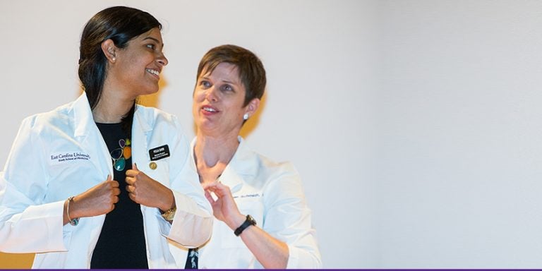 Incoming Brody School of Medicine student Pooja Sarin is helped into her white coat by Dr. Susan Schmidt, associate dean for Student Affairs. All 80 new students received a white coat as a gift from the BSOM Alumni Society to recognize their induction into the Brody medical alumni family. (Photos by Cliff Hollis)