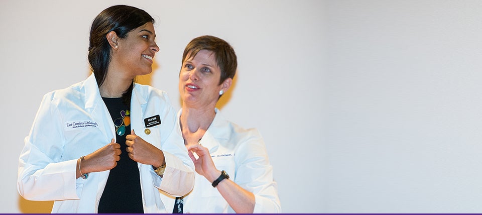 Incoming Brody School of Medicine student Pooja Sarin is helped into her white coat by Dr. Susan Schmidt, associate dean for Student Affairs. All 80 new students received a white coat as a gift from the BSOM Alumni Society to recognize their induction into the Brody medical alumni family. (Photos by Cliff Hollis)