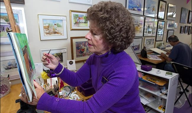 East Carolina University nursing professor Lou Everett paints an original watercolor as Pete Hickey works in the background at the Painting Purple & Other Colors Artists' Working Studio and Gallery. Hickey and the Groessers will open the shop for the first artist studio tour Nov. 5 to raise funds for scholarships in the ECU School of Art and Design. Photos by Cliff Hollis