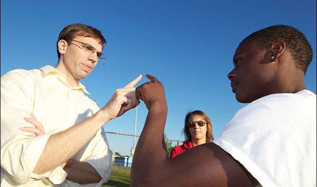 At far left, Dr. Brock Niceler, clinical assistant professor of family medicine at the Brody School of Medicine, performs a test for neurological wellness with a Rose High football player during afternoon practice. ECU graduate student Becky Grant, center, an athletic trainer assigned to Rose High School, looks on during the procedure. (Photo by Cliff Hollis)