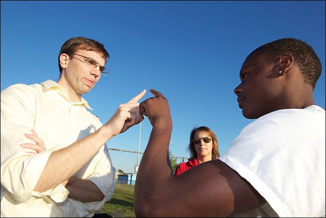 At far left, Dr. Brock Niceler, clinical assistant professor of family medicine at the Brody School of Medicine, performs a test for neurological wellness with a Rose High football player during afternoon practice. ECU graduate student Becky Grant, center, an athletic trainer assigned to Rose High School, looks on during the procedure. (Photo by Cliff Hollis)