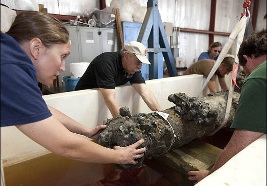 At left, Shanna Daniels, QAR project conservator steadies the cannon while Lawrence Babits, center, director of the ECU maritime studies program, and Charles Bowdoin, an ECU student at right, work to position the cannon on a block in the holding tank at ECU's QAR Conservation Lab. (Photos by Cliff Hollis)