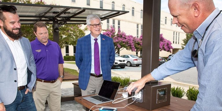 Sustainability Manager Chad Carwein, left, Recycling Coordinator Terry Little and Dr. Mark Stacy, dean of the Brody School of Medicine, listen as Eddie Johnson, assistant director of ECU’s Office of Prospective Health, discusses the functionality of newly installed solar tables at Brody. (Photo by Rhett Butler)