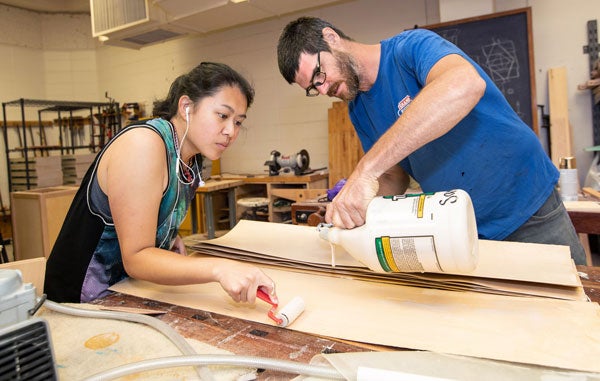 From left, ECU senior Christy Vang and instructor Judd Snapp work together to glue layers of veneer that will eventually become a skateboard. 
