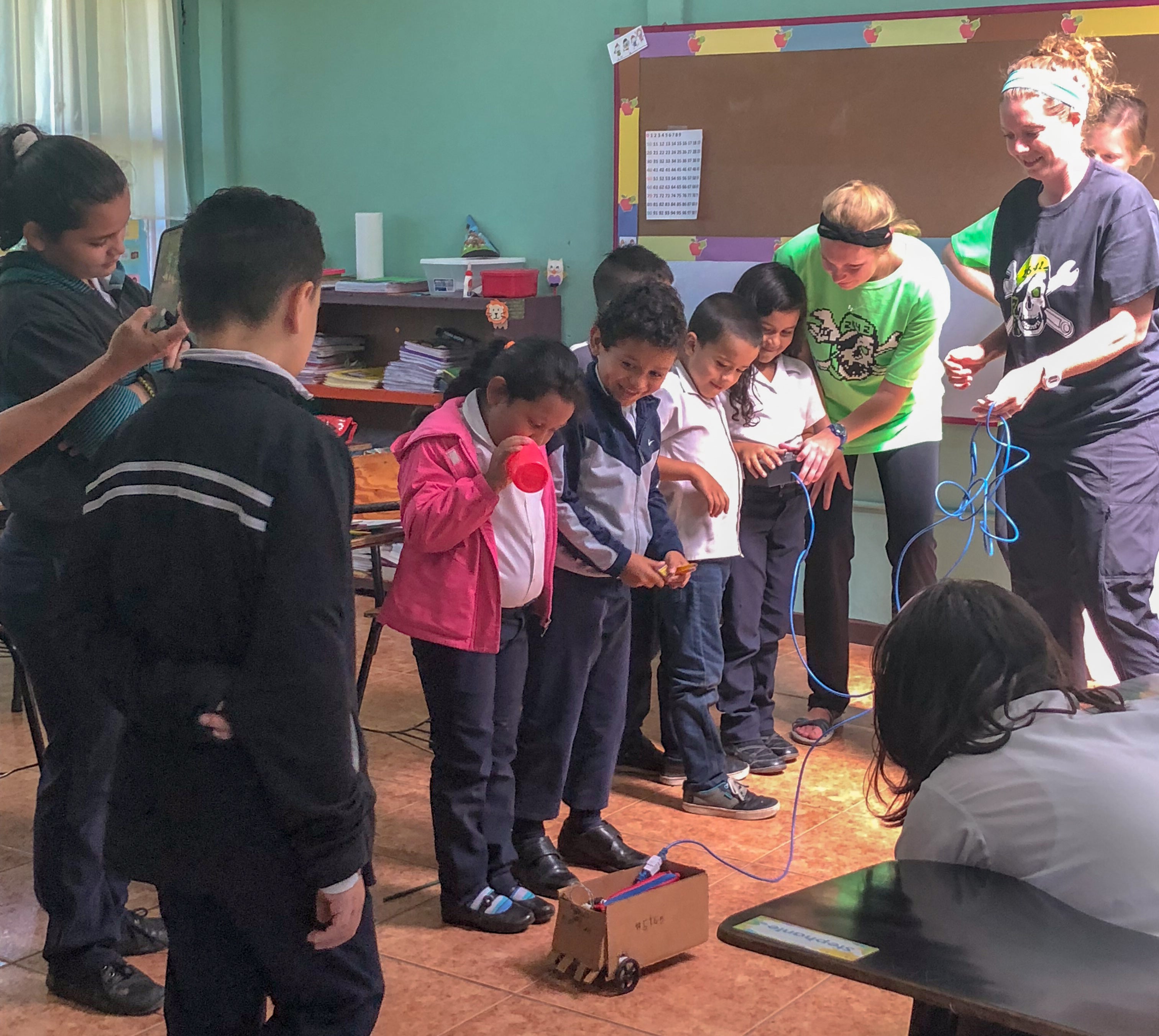 The graduate students show children at the school how to operate a robot made from repurposed cardboard.