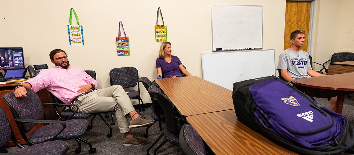 From left, ECU faculty members Todd Fraley and Stacy Warner watch a simulated scenario between ECU student-athlete Diogo Marques and his tennis coach avatar as they discuss returning from an injury.
