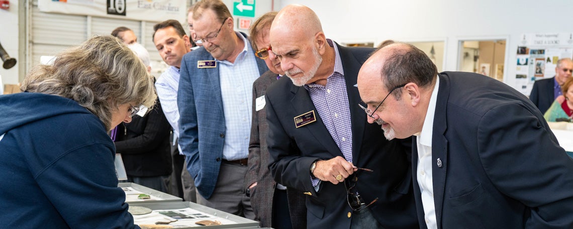Angus Konstam (right) looks on as Sarah Watkins-Kenney (left), from the QAR lab, describes artifacts retrieved from the Queen Anne’s Revenge. Also pictured (left to right) are ECU chemistry professor Jack Pender, and THCAS Dean’s Advancement Council members Phil Hodges, Wayne Holloman and Mitchell Hunt.