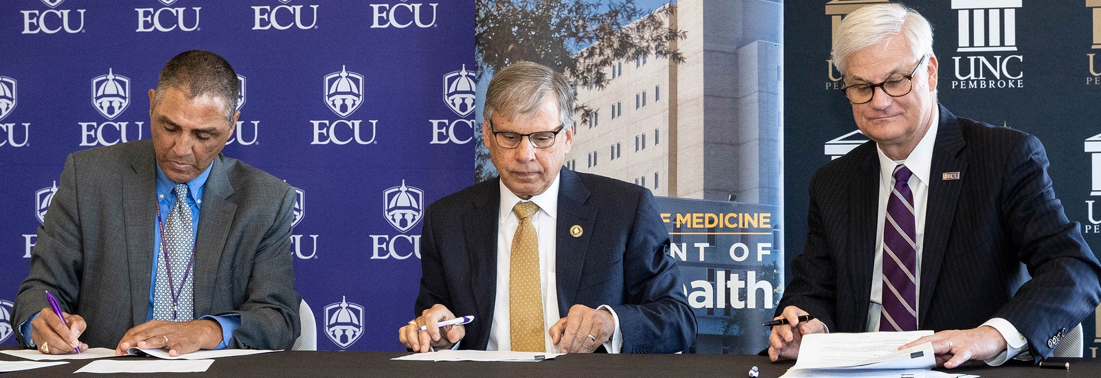(From left) Dr. Ronny Bell, chair of ECU’s Department of Public Health, UNC-Pembroke Chancellor Dr. Robin Gary Cummings and Dr. Mark Stacy, dean of ECU’s Brody School of Medicine, sign a memorandum of understanding on Dec. 6, 2018 to formalize a public health partnership between the two schools. (Photo by Cliff Hollis)