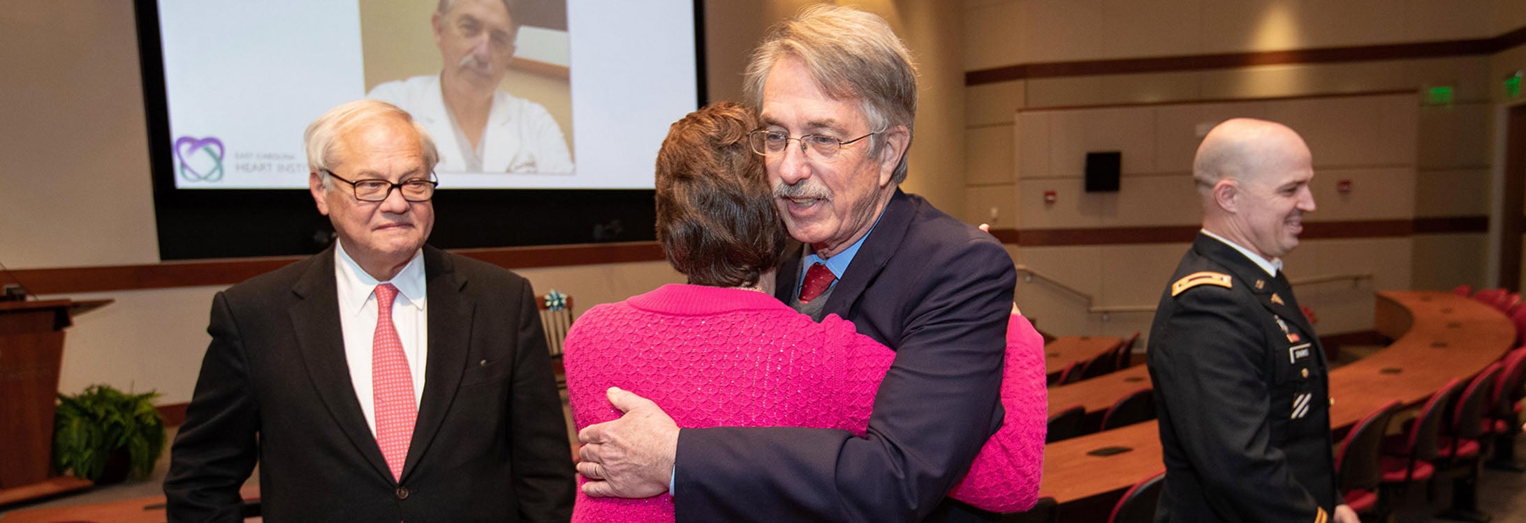 Dr. Mark Williams shares a hug with a friend after a ceremony for the establishment of the Travis and Cassandra Burt Professorship in Cardiovascular Sciences at the ECHI, as Dr. Randolph Chitwood, left, the founder and former head of ECHI, looks on. (Photos by Rhett Butler)