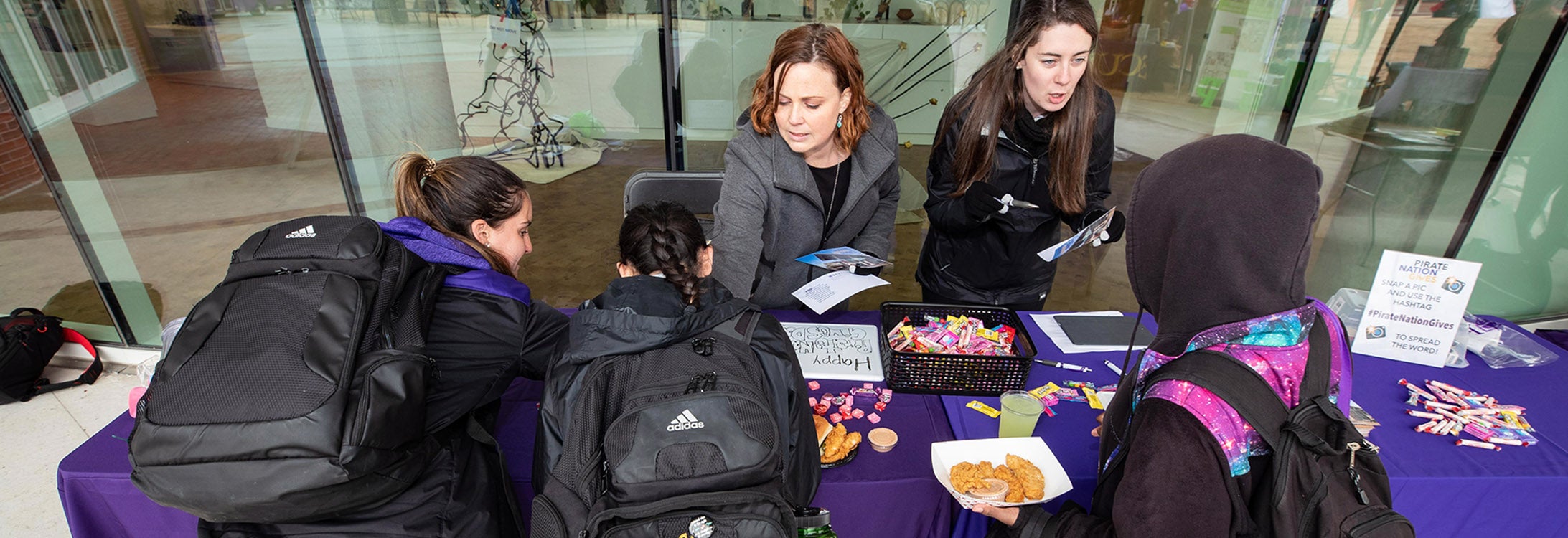 Associate Dean of Students Lauren Thorn, left, and Carter Morsell, donor relations coordinator for the Division of Student Affairs Office of Development, talks to students at the Pirate Nation Gives table outside of the Main Campus Student Center on Wednesday.