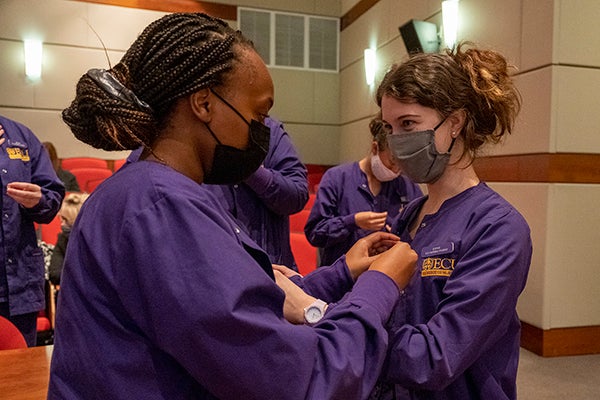 • Nursing students Priscilla Gichaca, left, and Sophie Giddings, pin each other with golden lamp pins. (Photo by Jeremy Smith, ECU College of Nursing)