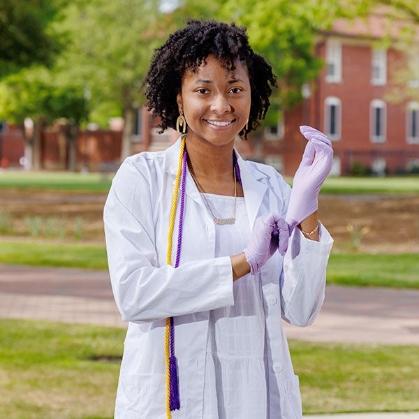 ECU graduate profile Dymon Blango poses with her lab coat on the mall.