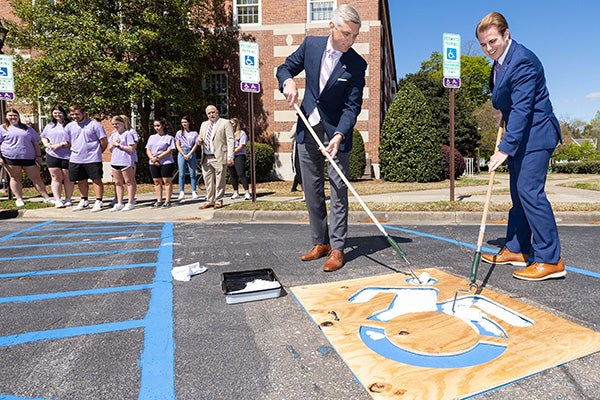 Chancellor Philip Rogers, left, and ECU student body president Chandler Ward paint a parking spot outside the Spilman Building to display an updated, more active accessible icon. 