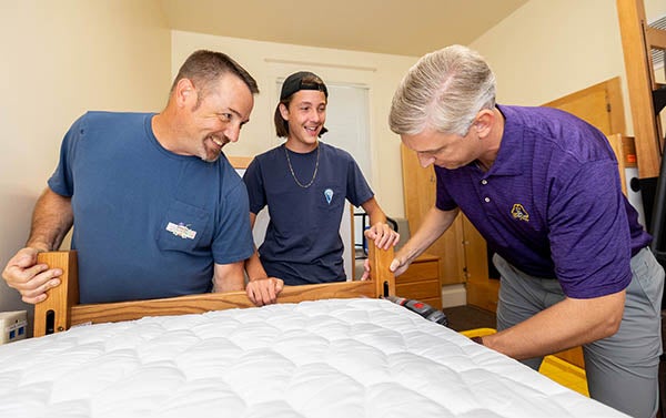 ECU Chancellor Philip Rogers, left, helps Jim Phipps, right, set up a bed for his son, Carson, in his dorm room. 