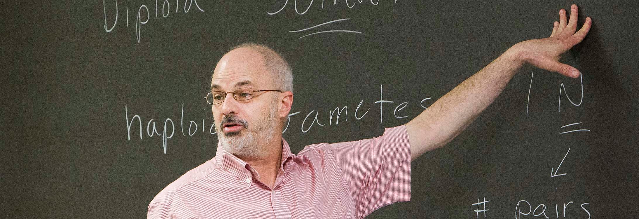 John Stiller points to a chalkboard in class.