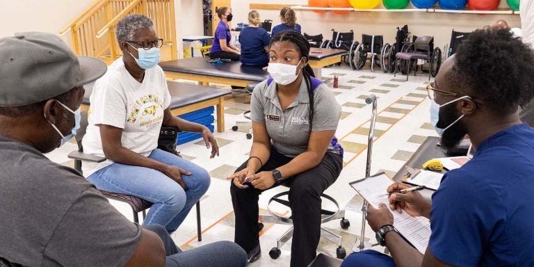 Physical Therapy student Junae Staples, and occupational therapy student Ayoola Ajani, in blue scrubs, work with a family during a student-run clinic for eastern North Carolina patients.