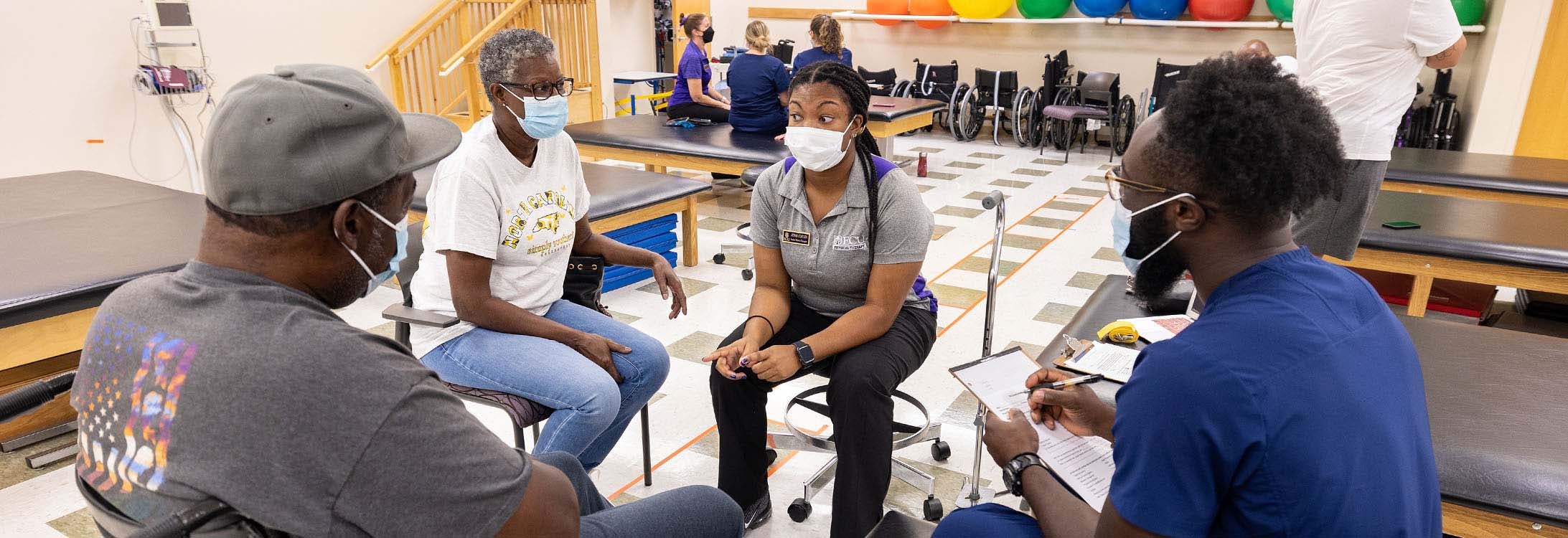 Physical Therapy student Junae Staples, and occupational therapy student Ayoola Ajani, in blue scrubs, work with a family during a student-run clinic for eastern North Carolina patients.